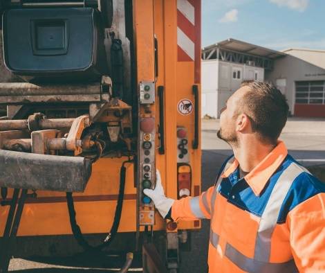 A bin man operating the lifting mechanism at rear of lorry.