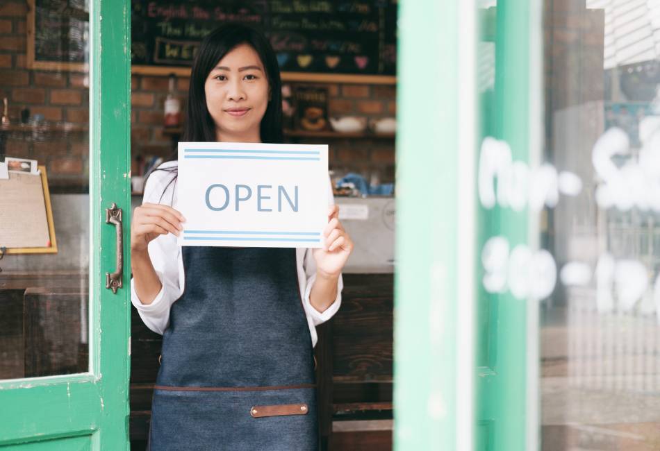 Cafe owner holding a sign showing her shop is open for business
