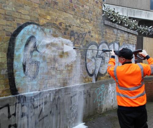 Man using jet hose to clean graffiti from a brick wall.