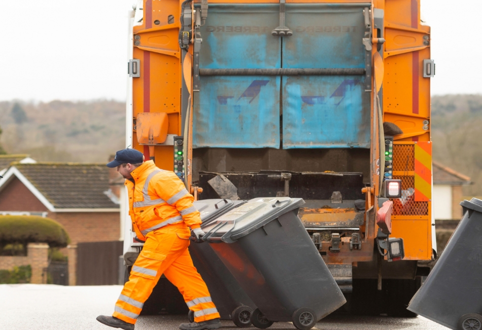 A bin man pulling bins away from a waste truck.