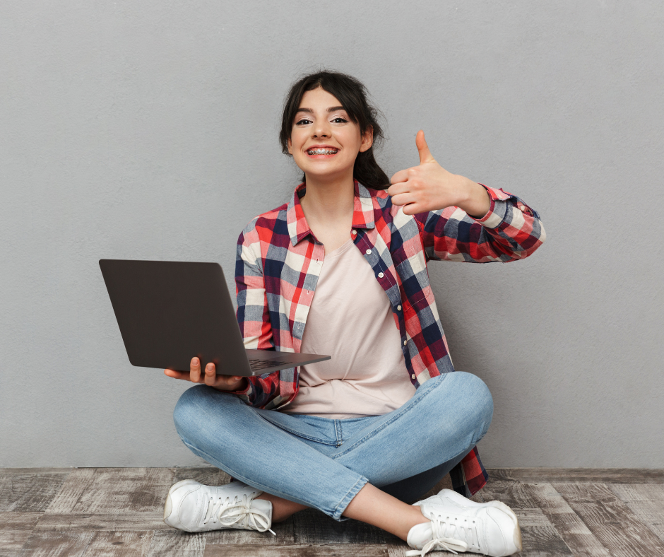 A girl sitting cross legged with a laptop and her thumb up.