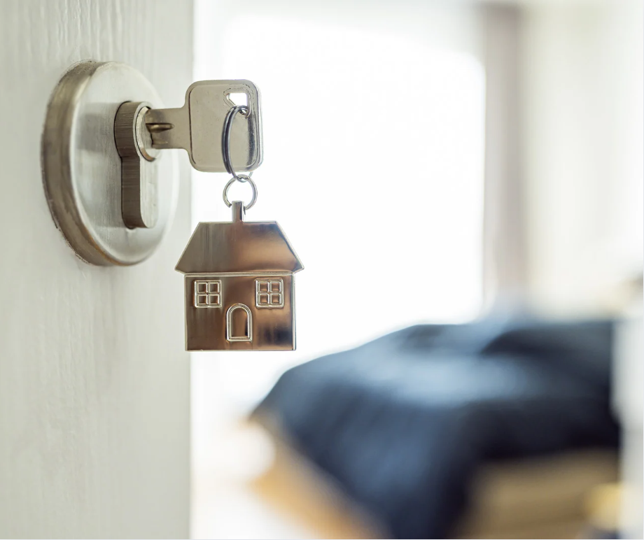 Keys in a door with a bed in the background.