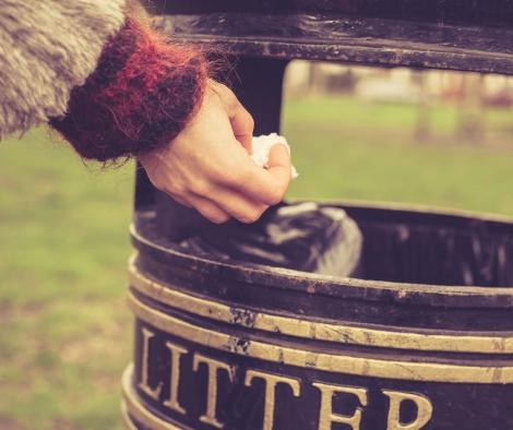 A hand depositing rubbish in a public bin.