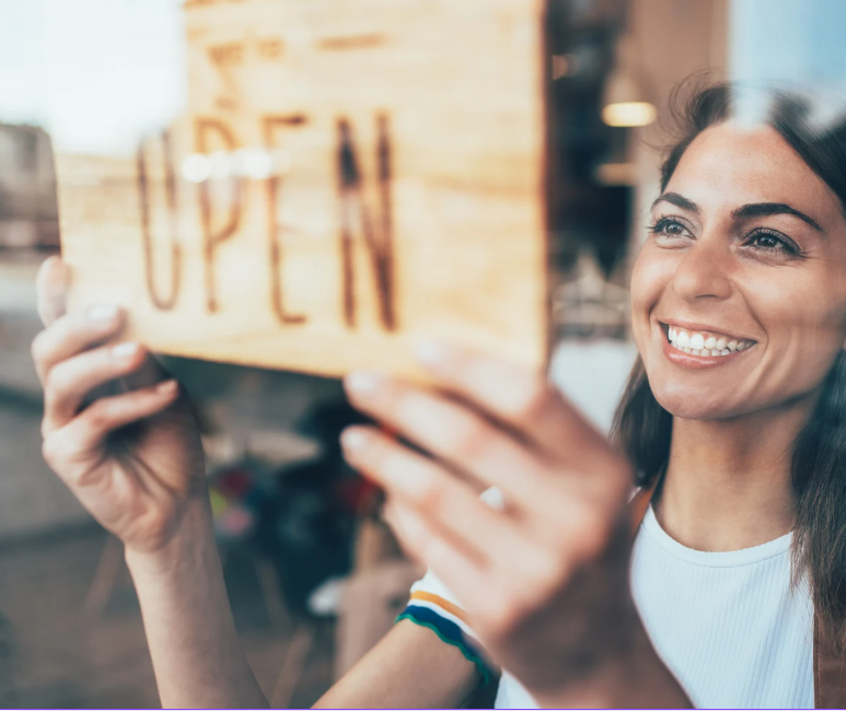 A smiling woman turning over an open sign on a shop door.