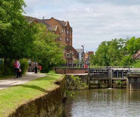 View looking along the river bank with pedestrian walking along path.