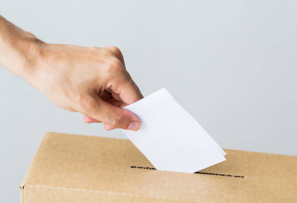 Hand posting a vote through a slot in a box