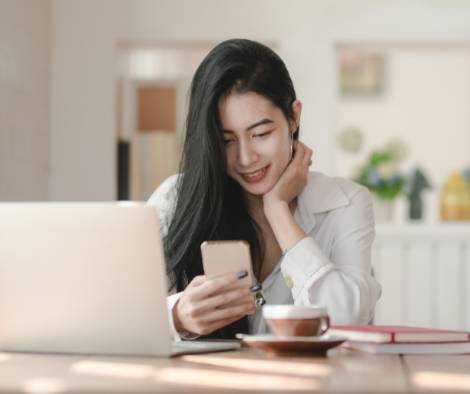 A woman with a mobile phone in her hand and a laptop open next to her